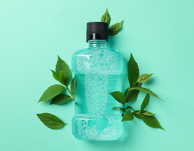 Mouthwash-and-leaves-on-mint-background,-space-for-text
